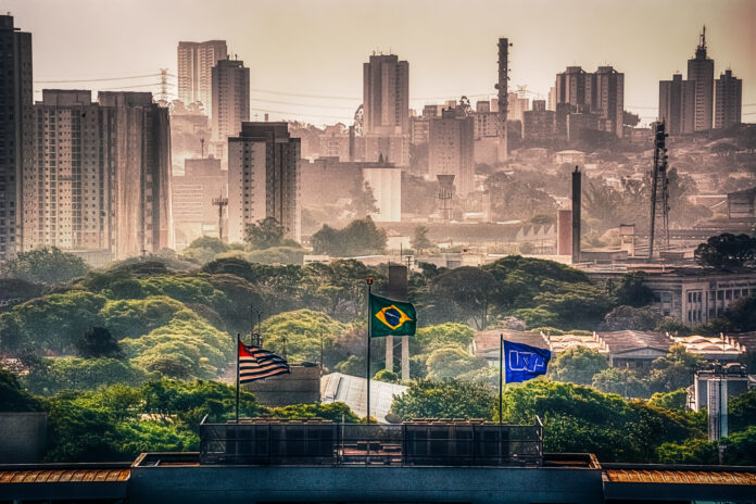 Bandeiras da cidade de São Paulo, do Brasil e da Universidade de São Paulo (eleita a mais sustentável da América Latina), lado a lado, da esquerda pra direita, hasteadas na parte de cima do prédio da antiga reitoria da USP.