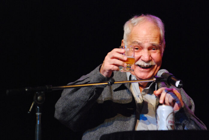 Paulo Vanzolini, em show na Virada Cultural em São Paulo, sorriso enquanto levanta um copo em direção a plateia.