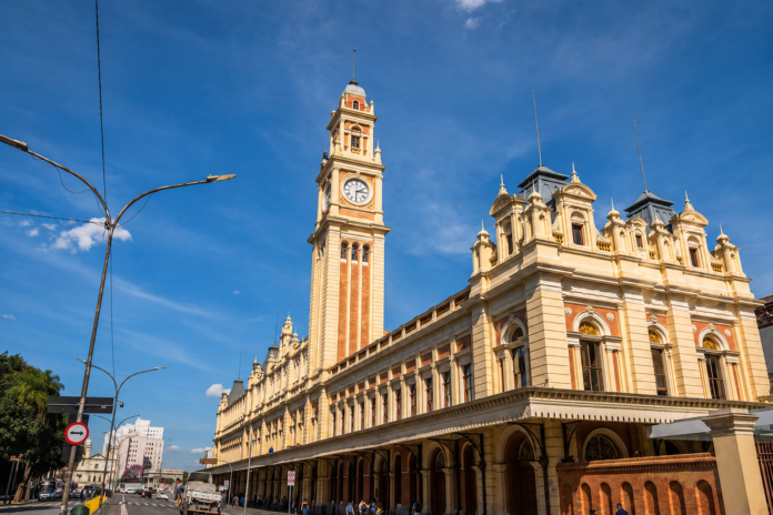Vista externa do Museu da Língua Portuguesa, na Estação da Luz, em São Paulo, com torre do relógio e céu azul ao fundo