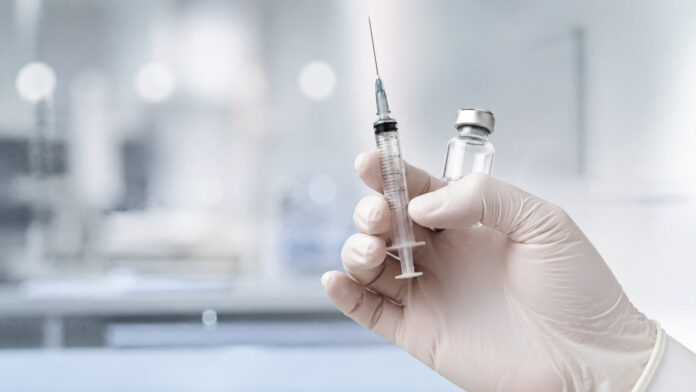 Mão com luva segura seringa e frasco de vacina em ambiente de laboratório