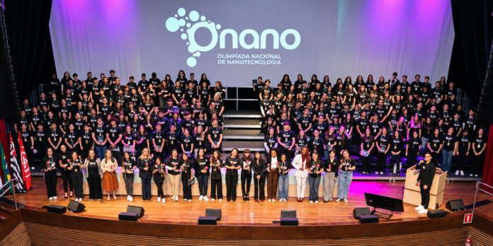 Estudantes e organizadores reunidos no palco durante cerimônia da Olimpíada Nacional de Nanotecnologia, com o logo da ONANO ao fundo
