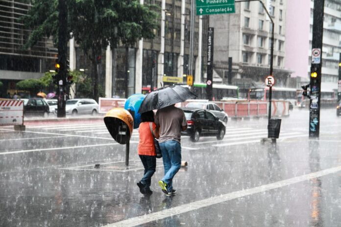Pessoas caminham sob chuva forte em área urbana