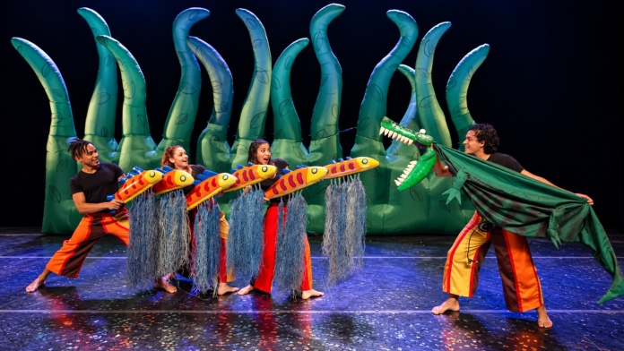Artistas manipulam bonecos de peixes coloridos e um jacaré durante espetáculo de teatro infantil